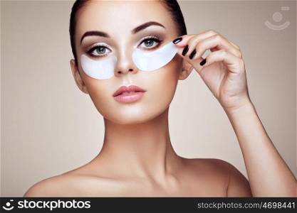 Portrait of Beauty Woman with eye Patches showing an effect of Perfect Skin. Beautiful Face of young Woman with clean Fresh Skin and bare shoulders on beige background. Brunette Spa Girl.