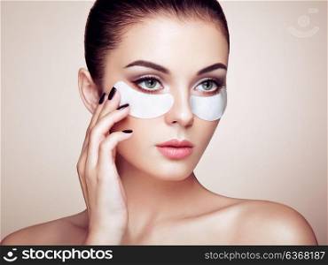 Portrait of Beauty Woman with eye Patches showing an effect of Perfect Skin. Beautiful Face of young Woman with clean Fresh Skin and bare shoulders on beige background. Brunette Spa Girl