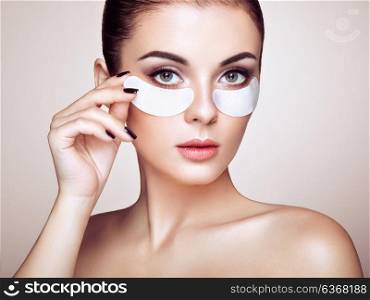 Portrait of Beauty Woman with eye Patches showing an effect of Perfect Skin. Beautiful Face of young Woman with clean Fresh Skin and bare shoulders on beige background. Brunette Spa Girl
