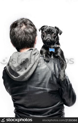 portrait of black pug and man, the pug is looking at the camera in the arms of the owner who is not facing the camera, the owner has a black hoodie.