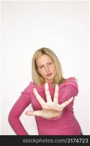 Portrait of blond Caucasian teen girl holding her hand out towards the viewer with attitude against white background.
