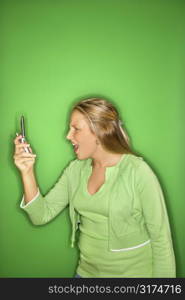 Portrait of blond Caucasian teen girl looking at cellphone with shock and disbelief against green background.