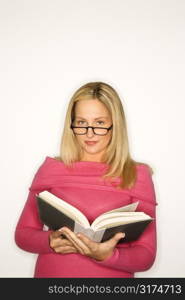Portrait of blond Caucasian teen girl wearing eyeglasses and holding a book looking at viewer.
