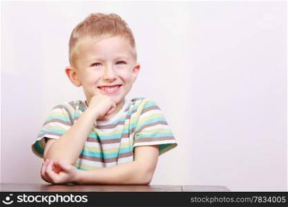 Portrait of blond cute happy laughing boy child kid at the table interior. Emotions and fun.