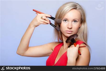 Portrait of blond girl holding professional makeup brushes on violet. Young woman as visagiste or stylist. Studio shot.
