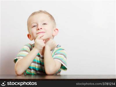 Portrait of blond pensive thoughtful boy child kid at the table indoor. Emotions and dreams. Blank copy space.