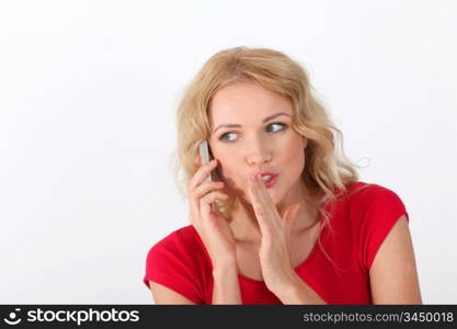 Portrait of blond woman with red shirt telling secret on the phone