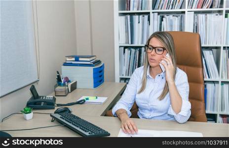 Portrait of blonde businesswoman talking with smartphone sitting in office. Blonde businesswoman talking with phone in the office