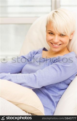 Portrait of blonde smiling woman sitting on the sofa at home