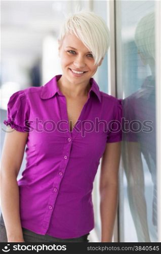 Portrait of blonde smiling woman standing next to a glass wall