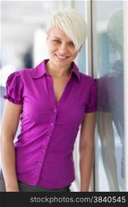 Portrait of blonde smiling woman standing next to a glass wall