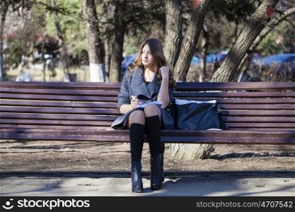 Portrait of blonde young schoolgirl sitting on the bench in spring park