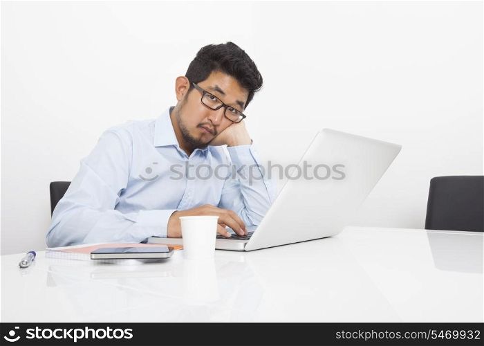Portrait of bored businessman sitting with laptop at desk in office