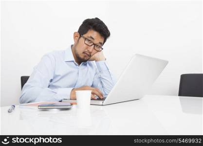 Portrait of bored businessman sitting with laptop at desk in office