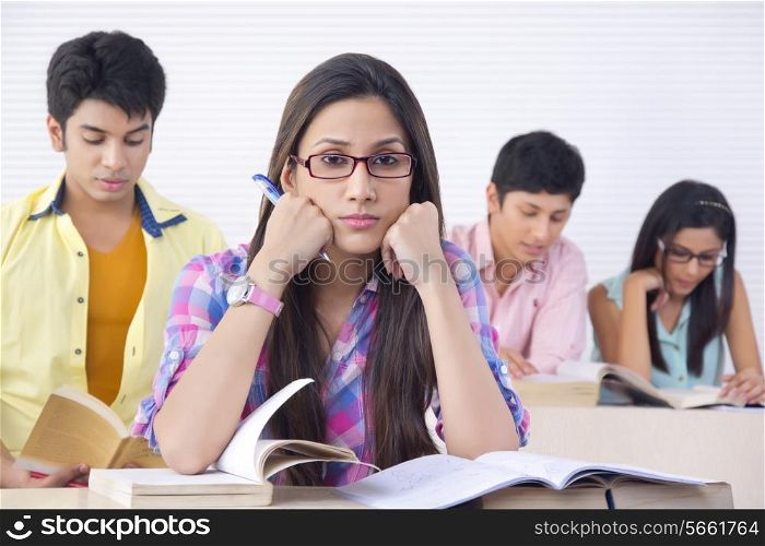 Portrait of bored college student with friends studying in background at classroom