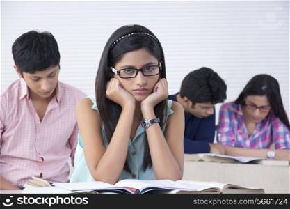 Portrait of bored female student with friends in background at classroom