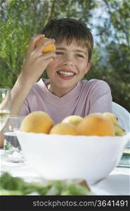Portrait of boy (10-12) eating peach at garden table, smiling