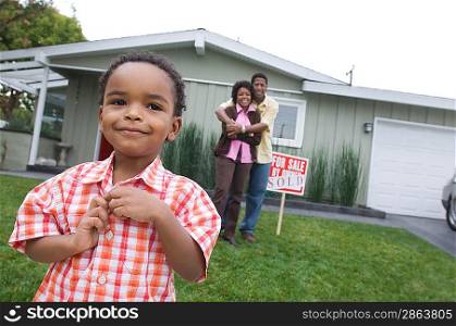 Portrait of boy (5-6) in front of new house, parents in background