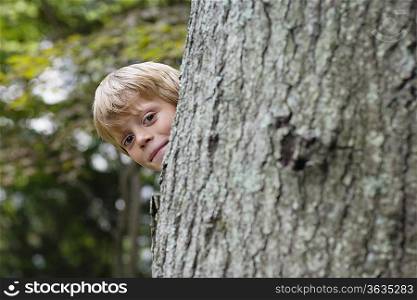 Portrait of boy (5-6) peeking from behind tree, smiling
