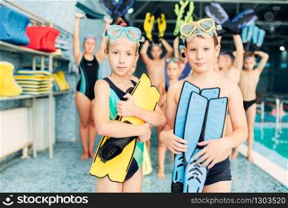 Portrait of boy and girl with colorful flippers in hands near swimming pool. Sportive healthy children after swimming exercises. Happy kids in modern sport center.. Portrait of boy and girl with colorful flippers