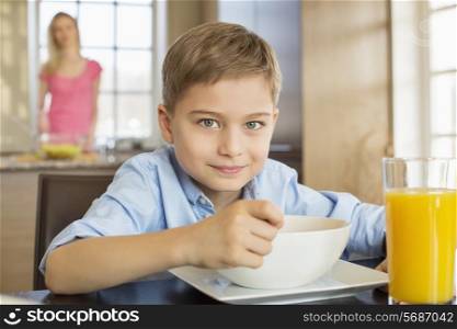 Portrait of boy having breakfast at table with mother standing in background