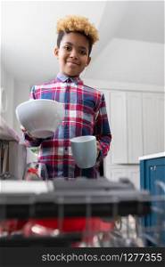 Portrait Of Boy Helping With Chores At Home By Stacking Crockery In Dishwasher