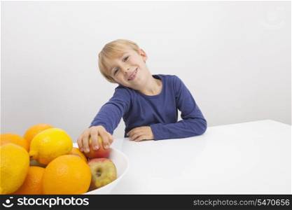 Portrait of boy holding apple from fruit bowl at table