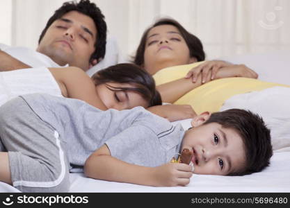 Portrait of boy holding chocolate while his family sleeping in the background