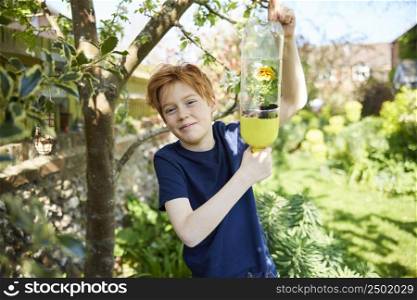 Portrait Of Boy Making Recycled Plant Holder From Plastic Bottle Waste In Garden At Home