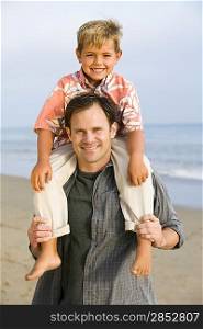 Portrait of boy on fathers shoulders at beach