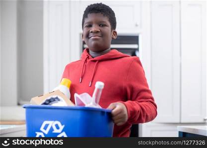 Portrait Of Boy Standing In Kitchen At Home Carrying Recycling Bin