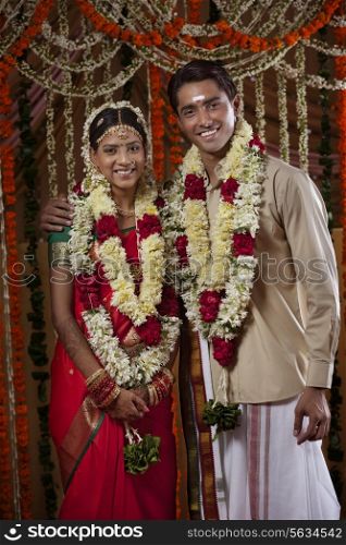 Portrait of bride and groom wearing garlands during traditional Indian wedding