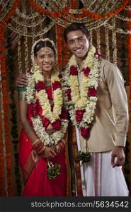 Portrait of bride and groom wearing garlands during traditional Indian wedding
