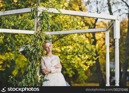 Portrait of bride standing near the overgrown plants of the gazebo.. Portrait of a bride in a white dress on background of a garden gazebo ent
