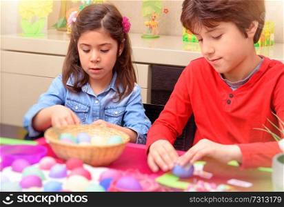 
Portrait of brother and sister painting traditional Easter eggs in different colors at home, with pleasure preparing to religious spring holiday