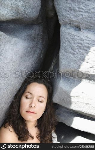 Portrait of brunette Caucasian mid-adult woman by rock formation with eyes closed.