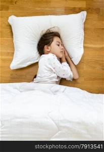 Portrait of brunette little girl sleeping on floor covered with blanket