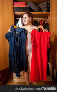 Portrait of brunette woman choosing between red and blue dress