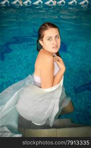 Portrait of brunette woman standing in pool and covering with white cloth