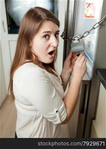 Portrait of brunette woman trying to open lock on fridge