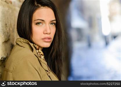 Portrait of brunette young woman with green eyes, wearing a coat, in urban background