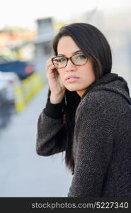 Portrait of brunette young woman with green eyes, wearing eyeglasses, in urban background