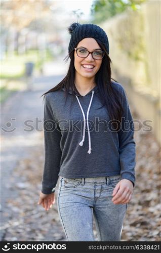 Portrait of brunette young woman with green eyes, wearing green casual clothes, eye glasses and hat, in urban background