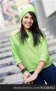 Portrait of brunette young woman with green eyes, wearing green casual clothes and hat, in urban background