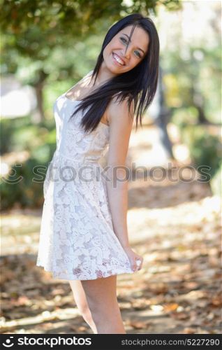 Portrait of brunette young woman with green eyes, wearing white dress, in urban park