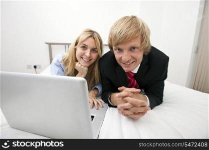 Portrait of business couple with laptop lying on bed