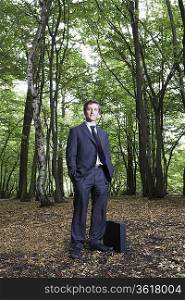 Portrait of business man in forest, hands in pockets