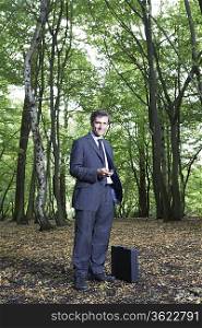 Portrait of business man in forest, holding mobile phone, smiling
