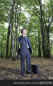 Portrait of business man in forest, talking on mobile phone