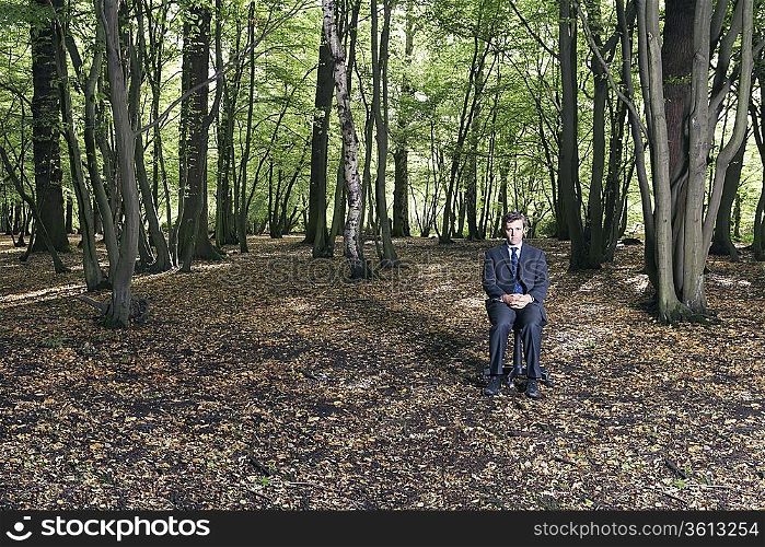 Portrait of business man sitting on office chair in middle of forest
